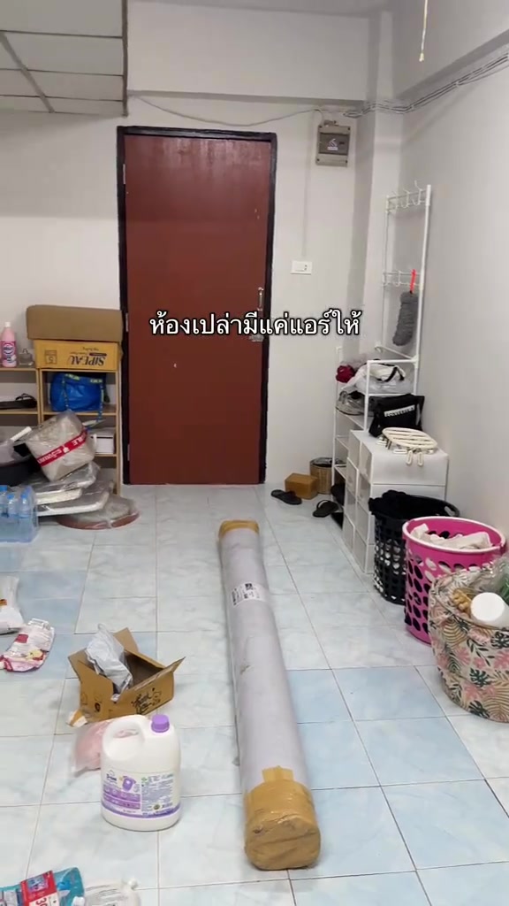ห้องเช่าเปล่าที่มีแค่แอร์ติดผนัง ของยังไม่ได้แกะและเสื่อน้ำมันยังม้วนวางกลางพื้นกระเบื้อง
