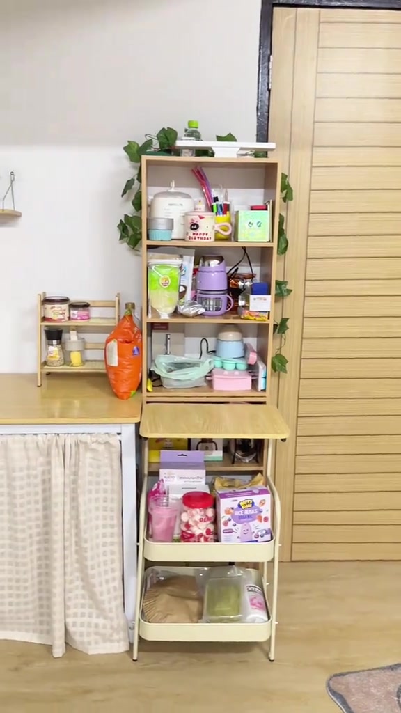 ชั้นไม้เก็บของจุกจิกในมุมครัวข้างตู้ที่ปิดด้วยผ้า skirt บนพื้นลายไม้สีอ่อน