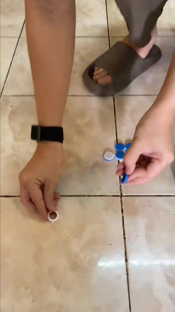 มือกำลังวางถ้วยเจลเหยื่อเล็ก ๆ ลงบนร่องยาแนวพื้นกระเบื้อง ข้าง ๆ มีแถบถ้วยฝาฟ้าที่ยังไม่ได้เปิด