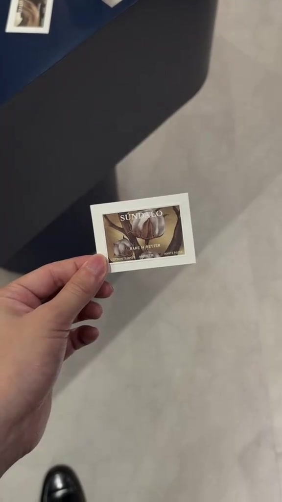 มือถือการ์ดทดสอบกลิ่น SÚNDALO กลิ่น Bare N'Better ลายดอกฝ้ายพื้นหลังเคาน์เตอร์สีน้ำเงิน