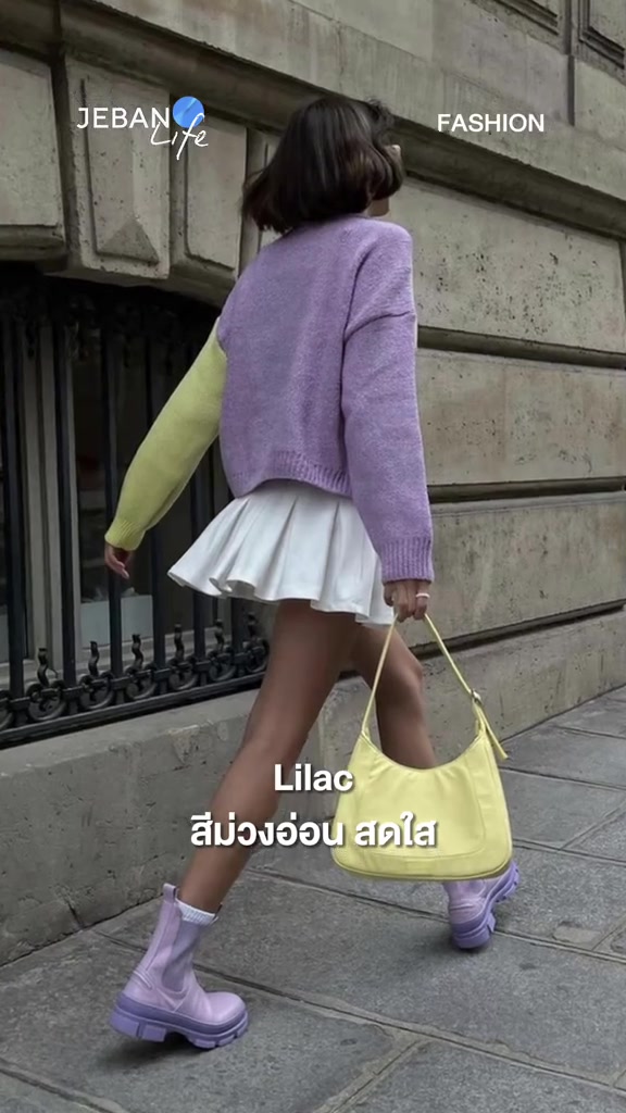 มุมมองด้านหลังของสาวที่สวมเสื้อไหมพรมสีไลแลคกับกระโปรงขาวและกระเป๋าสะพายสีเหลืองอ่อนบนทางเท้า