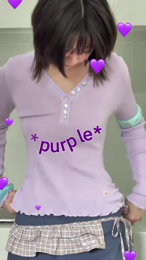 เสื้อแขนยาวสีม่วงอ่อนคอกระดุมถ่ายครอปตั้งแต่ช่วงหน้าลงมากับชายเสื้อขอบหยักและผ้าลายตารางซ้อนที่เอว