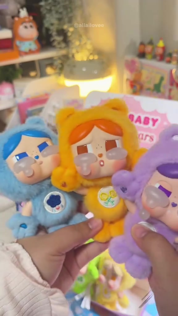 ตุ๊กตาหอย CRYBABY × Care Bears สามตัวสีน้ำเงิน เหลือง และม่วงถือเรียงกันในมือ