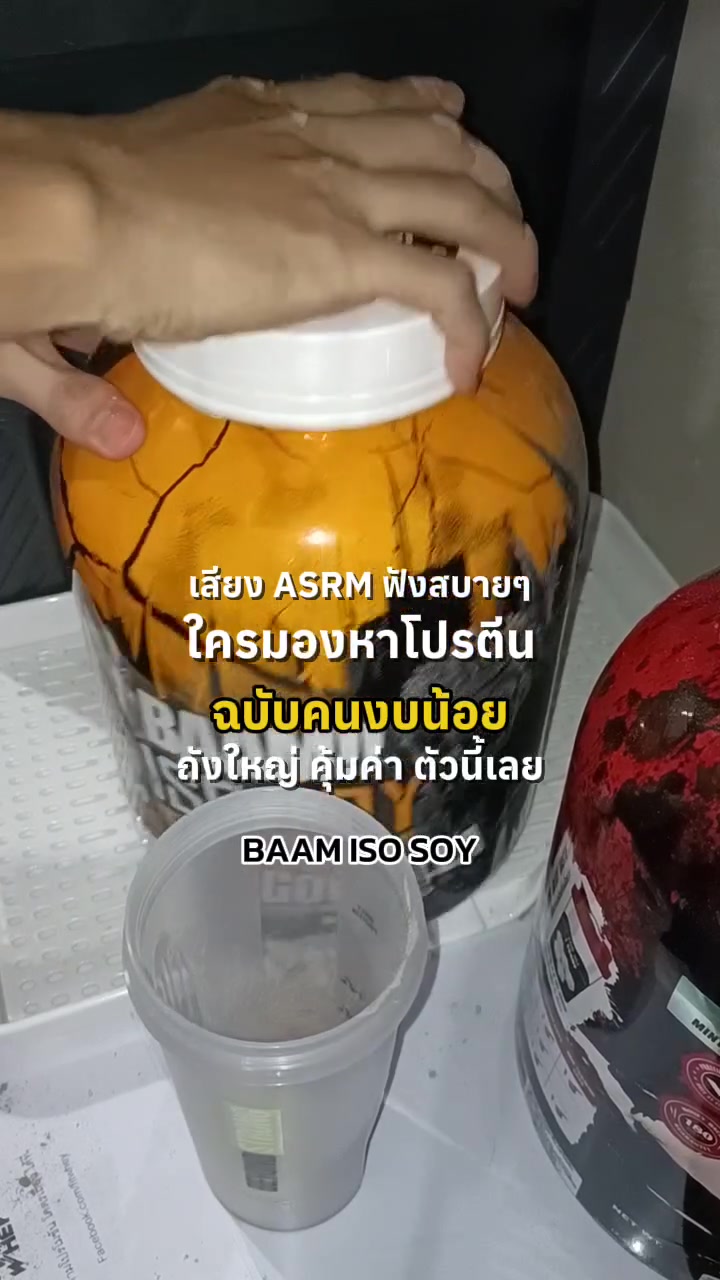 มือวางฝาปิดถังโปรตีน BAAM ISO SOY สีส้ม ด้านหน้ามีแก้วเชคใส่ผงโปรตีนไว้