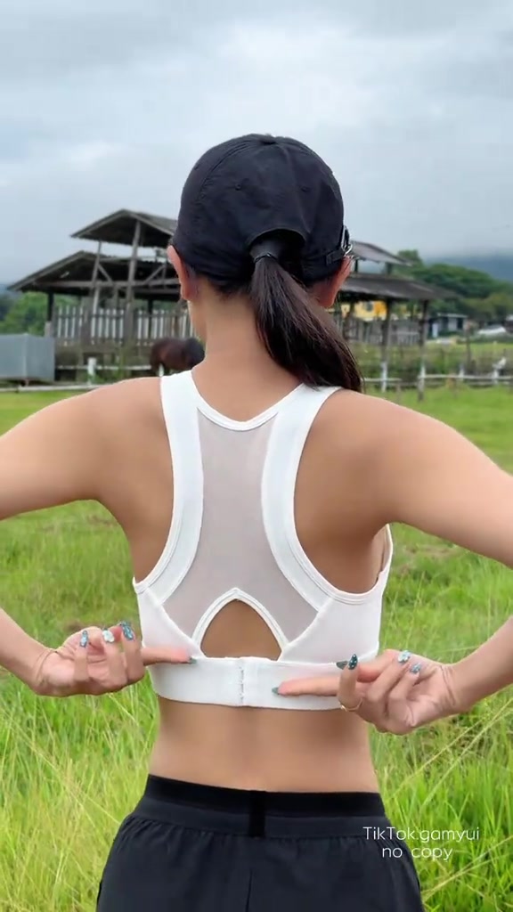 มุมมองด้านหลังของผู้ใส่สปอร์ตบราสีขาว เห็นแผงตาข่ายระบายอากาศและนิ้วชี้ที่แถบตะขอหลัง