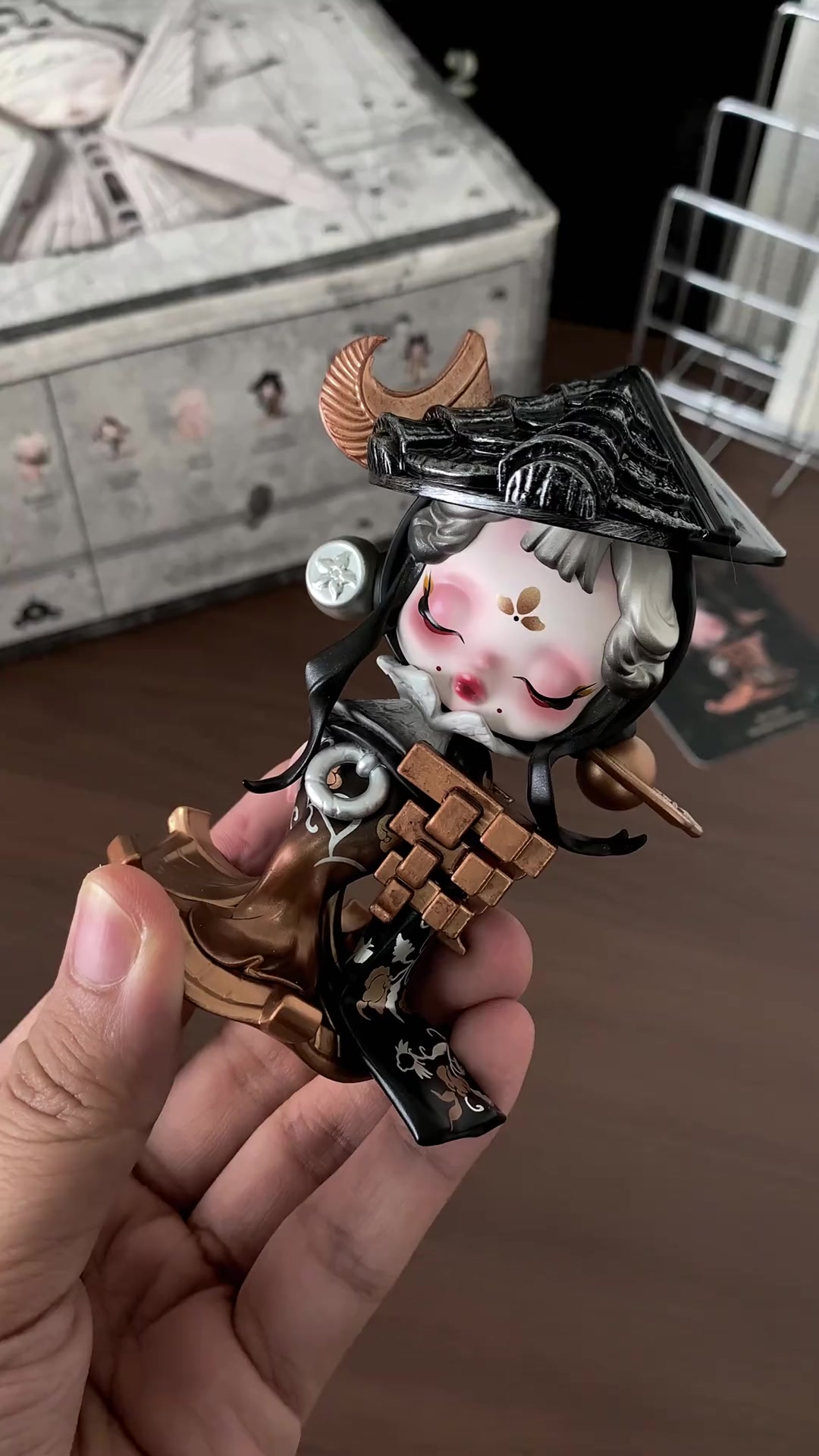 ฟิกเกอร์ SKULLPANDA Where Time Dwells โทนอารยธรรมจีนหลังคากระเบื้องดำถือบนมือ โดยมีกล่องซีรีส์วางอยู่ฉากหลัง