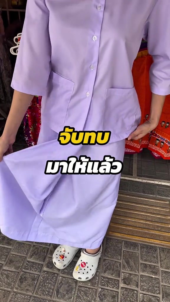 ชุดเซตสีอ่อนทรงสุภาพ เสื้อแขนสามส่วนมีกระดุมหน้าคู่กับผ้าถุงยาว ถ่ายตั้งแต่คอลงมาหน้าร้านเสื้อผ้า