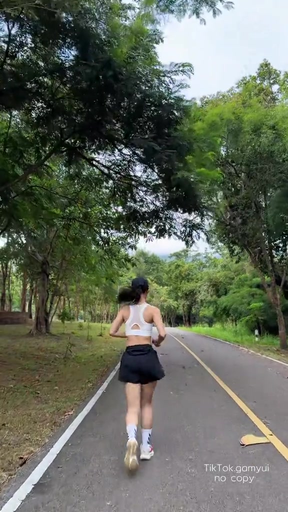 มุมมองด้านหลังของผู้ใส่สปอร์ตบราสีขาวกำลังวิ่งบนถนนริมทุ่ง แถบหลังแนบสนิทไม่เลื่อนขึ้น