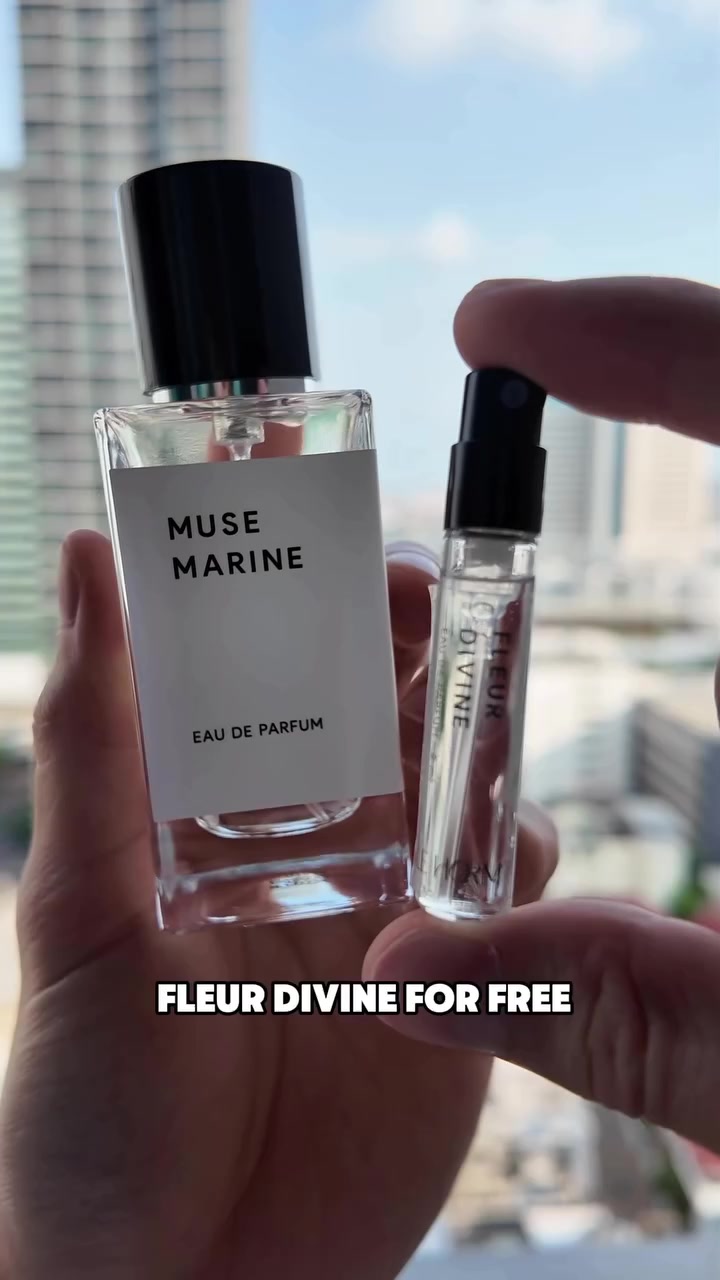 มือถือขวดน้ำหอม LE HORM Muse Marine ฉลากขาวคู่กับหลอดทดลองกลิ่นเล็กพื้นหลังเป็นท้องฟ้าและตึกสูง