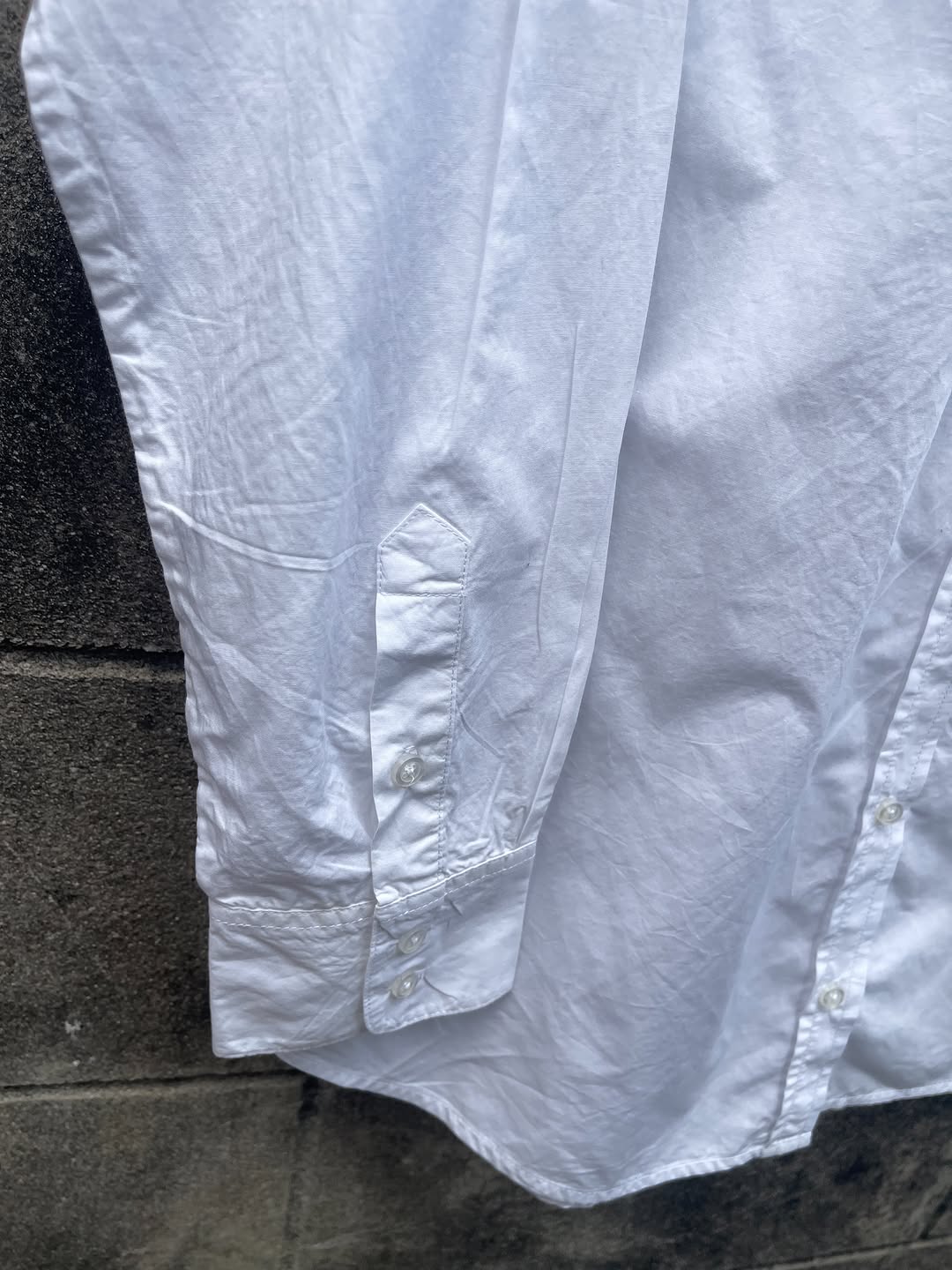 ภาพใกล้ของแขนและปลายแขนเสื้อเชิ้ตสีขาว เห็นเนื้อผ้าฝ้ายทอและกระดุมข้อมือชัด