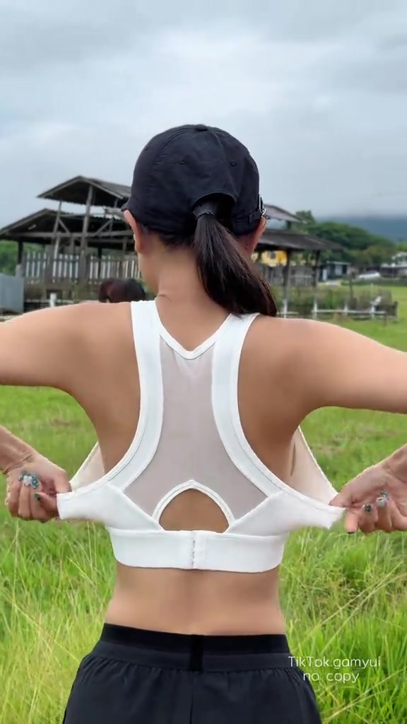 มือสองข้างดึงแถบหลังของสปอร์ตบราสีขาวให้ยืดออก เห็นแนวตะขอหลังกลางหลัง