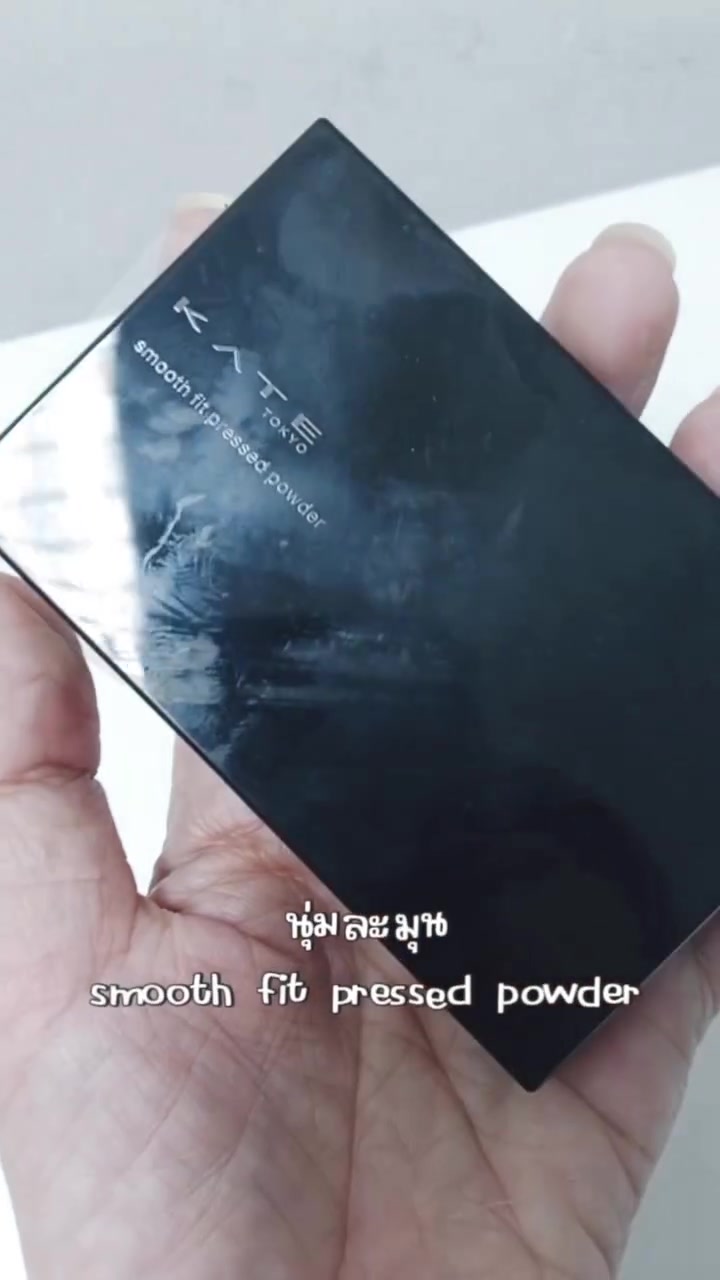มือถือตลับแป้งเคท สมูธ ฟิต เพรสส์ พาวเดอร์ สีดำมันวาว เห็นโลโก้และชื่อรุ่นบนฝา