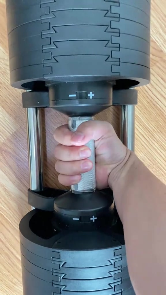 มือกำด้ามจับเหล็กชุบของดัมเบลปรับน้ำหนักที่ยกขึ้นจากฐานแล้ว เห็นเนื้อโลหะลายกันลื่นชัด