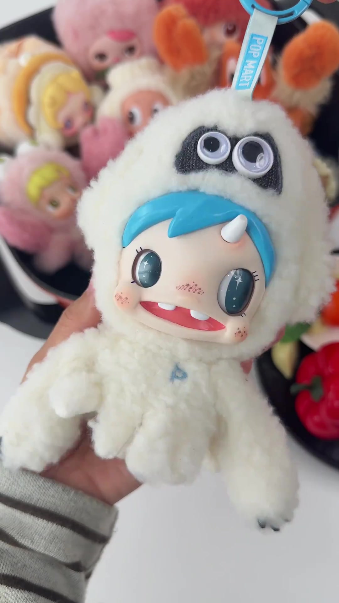 ตุ๊กตาพลัชฮู้ดขาวขนฟูผมฟ้าเขาเดียว ตาเป็นประกายดาว พร้อมสายห้อยสีฟ้าพิมพ์โลโก้และห่วงคลิปด้านบน