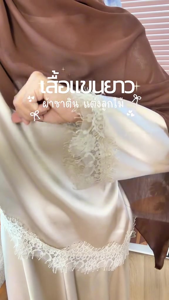 ภาพใกล้ของผ้าซาตินสีครีมแต่งขอบลูกไม้ที่ปลายแขน เห็นความเงาและการทิ้งตัวของเนื้อผ้า