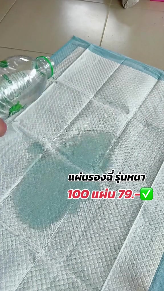 แผ่นรองฉี่ใช้แล้วทิ้งปูบนพื้นกระเบื้อง กำลังถูกเทน้ำจากขวดเพื่อทดสอบการซึมซับ