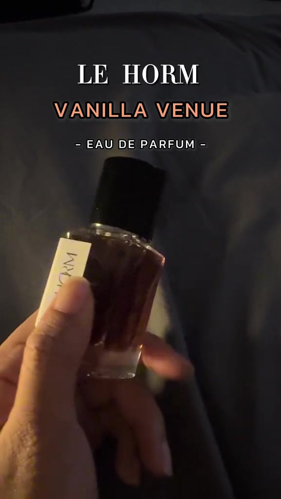 มือถือขวดน้ำหอม LE HORM Vanilla Venue ขนาดเล็ก น้ำหอมสีอำพันเข้ม ฝาดำ ฉากหลังเป็นผ้าสีเทา