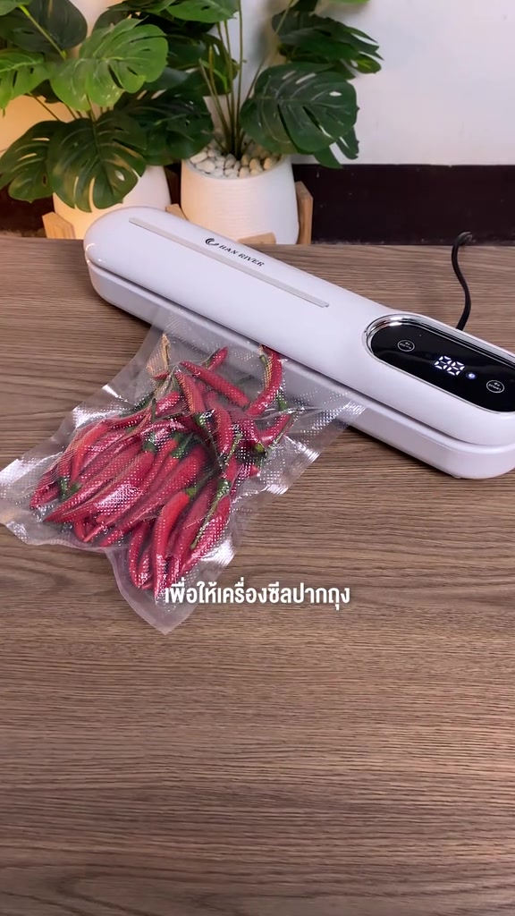 เครื่องซีลสูญญากาศสีขาวจอแอลอีดีนับเวลา ถุงลายนูนใส่พริกแดงถูกดูดแนบสนิทวางอยู่บนโต๊ะไม้
