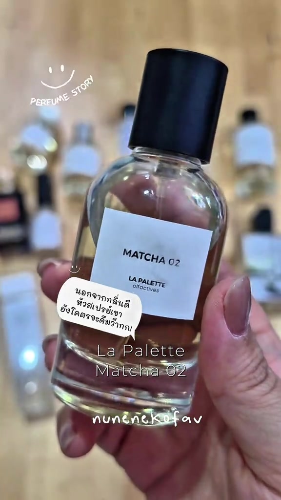 มือถือขวดน้ำหอม La Palette ฉลากขาวอ่านว่า MATCHA 02 พื้นหลังเป็นชั้นไม้