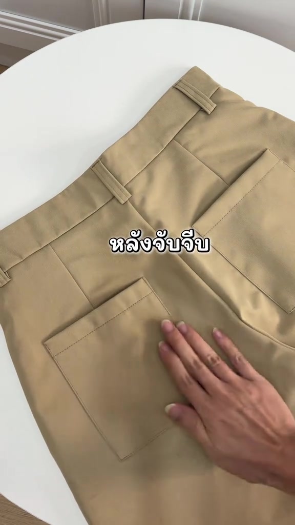 ด้านหลังกางเกงเบอร์มิวดาสีกากี เอวจับจีบและมีกระเป๋าแปะสองข้าง มือวางบนผ้า