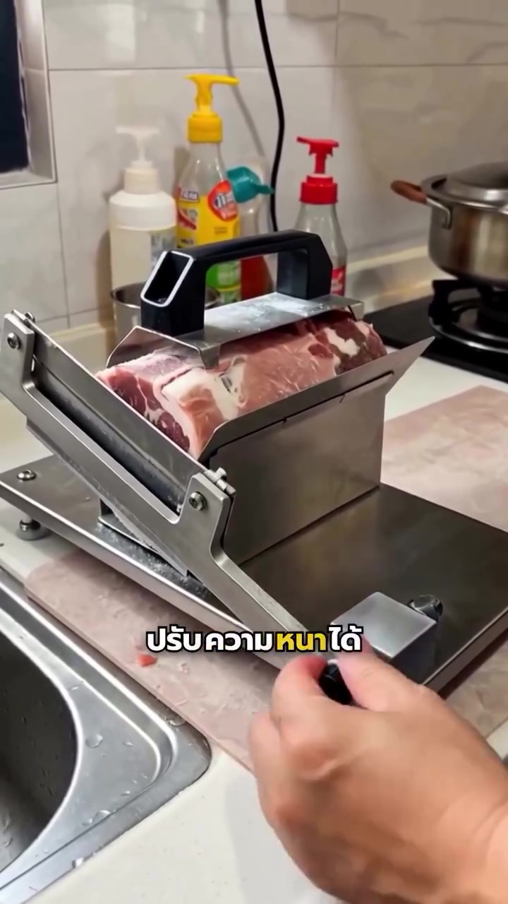 ที่สไลด์เนื้อแบบมือโยกมีก้อนหมูวางบนแท่นกด มือกำลังจับด้ามโยกใบมีดอยู่ข้างเครื่องบนเคาน์เตอร์ครัว