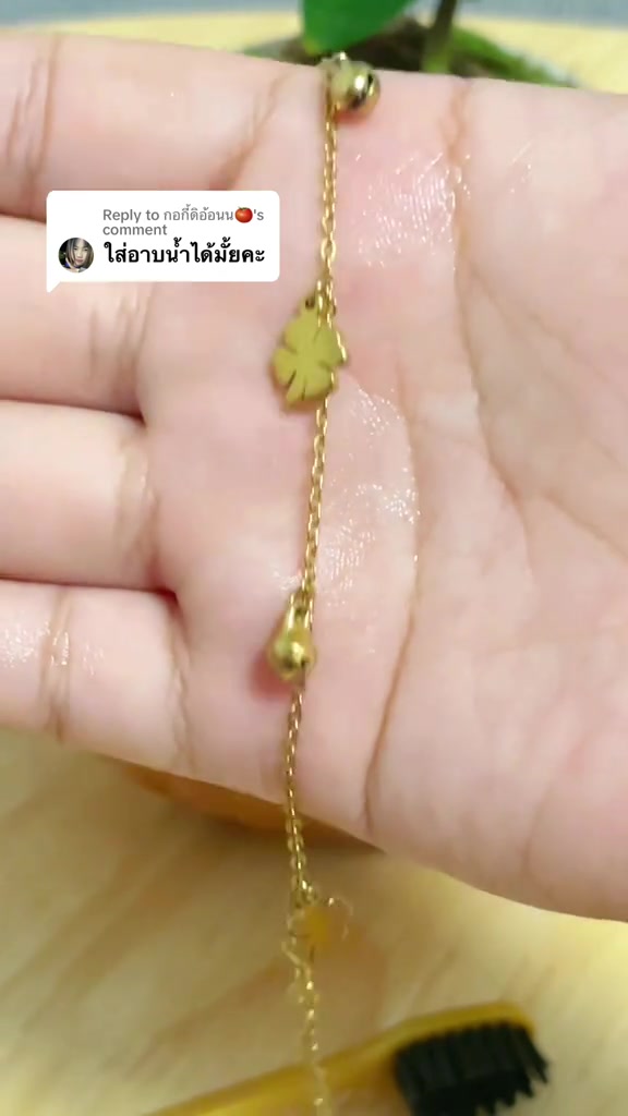 สร้อยข้อเท้าสแตนเลสชุบทองมีจี้กระดิ่งและจี้ใบไม้วางบนฝ่ามือพร้อมหยดน้ำหลังทดสอบโดนน้ำ