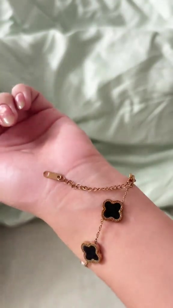 สร้อยข้อมือสีทองกุหลาบประดับใบโคลเวอร์สีดำวางพาดฝ่ามือ เห็นโซ่ต่อขยายและตัวล็อกชัดเจน