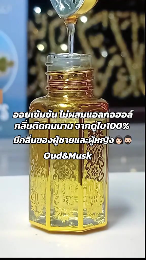 ออยล์สีทองถูกหยดจากหลอดหยดลงขวดแก้วลายทองแบบอาหรับที่ตั้งบนโต๊ะขาว