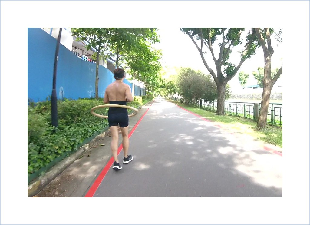 ภาพด้านหลังของผู้ชายที่วิ่งจ็อกกิงบนทางเดินในสวนสาธารณะโดยมีฮูลาฮูปหมุนรอบเอว