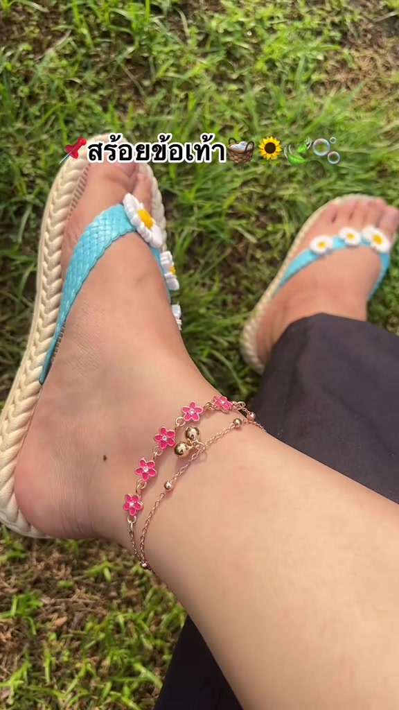 สร้อยข้อเท้าโซ่สองชั้นจี้ดอกไม้สีชมพูและกระดิ่งทองสวมบนข้อเท้าทั้งสองข้างคู่กับรองเท้าแตะดอกเดซี