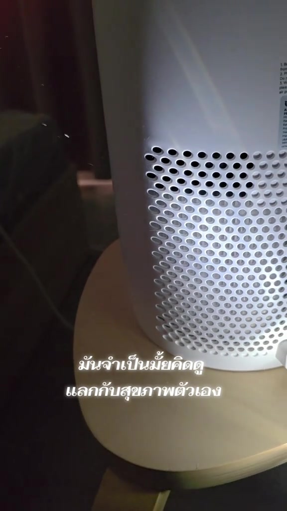 ระยะใกล้ของช่องดูดอากาศด้านข้างเครื่องฟอกอากาศทรงกระบอกสีขาวที่วางบนเก้าอี้ไม้