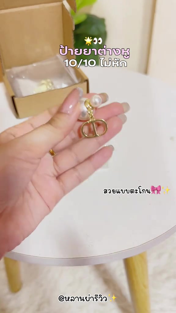 มือถือต่างหูมุกตัวล็อกสีทองเหนือกล่องกระดาษเปิดที่มีซองใส่เครื่องประดับวางอยู่ด้านใน