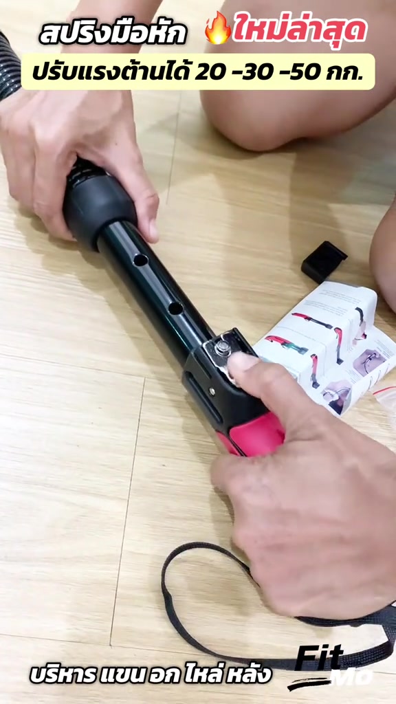 มือกดปุ่มล็อกปรับแรงต้านที่ด้ามของสปริงมือหักด้ามสีชมพูที่วางบนพื้นไม้