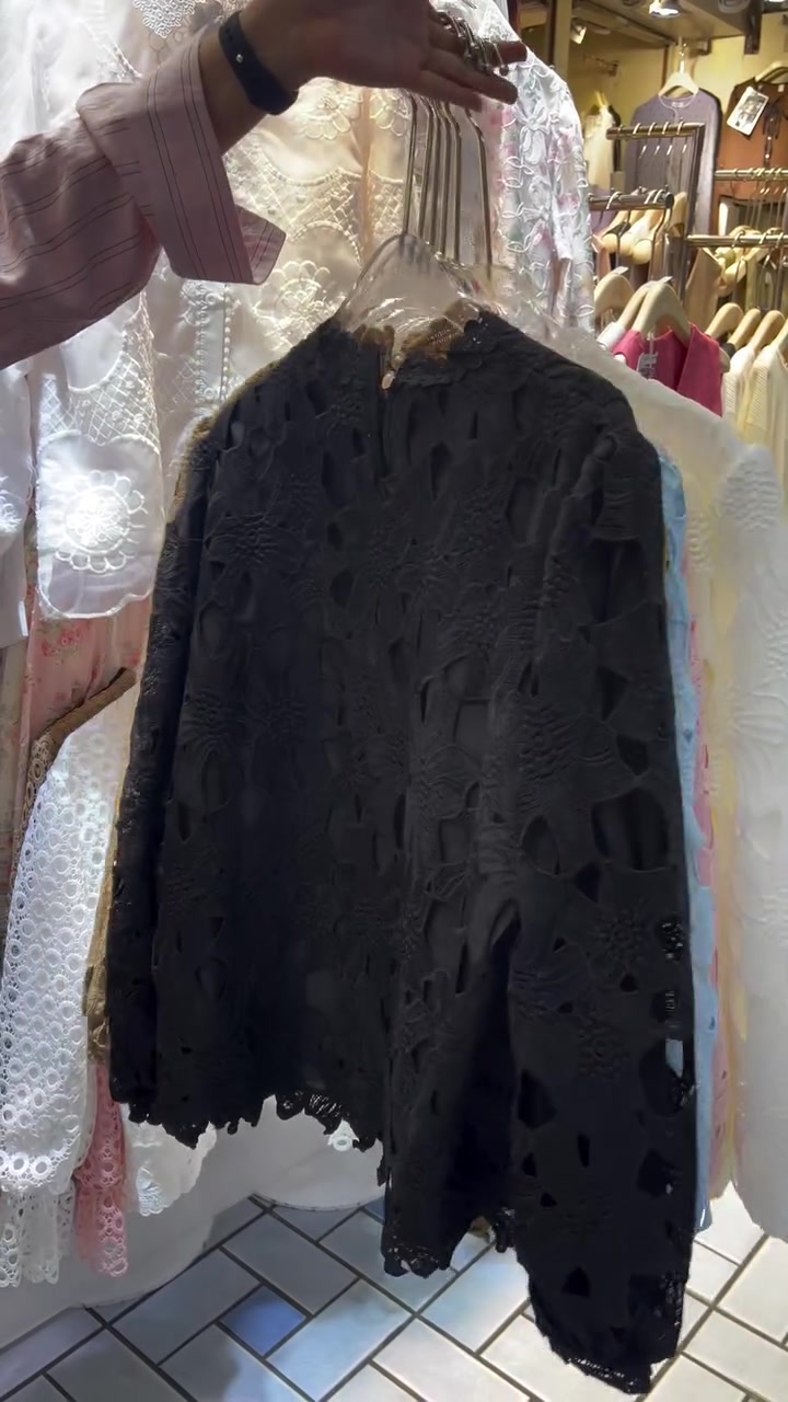 เสื้อลูกไม้ฉลุสีดำแขวนบนไม้แขวน เห็นลายเจาะโปร่งทั่วตัวเสื้อและชายเสื้อหยัก
