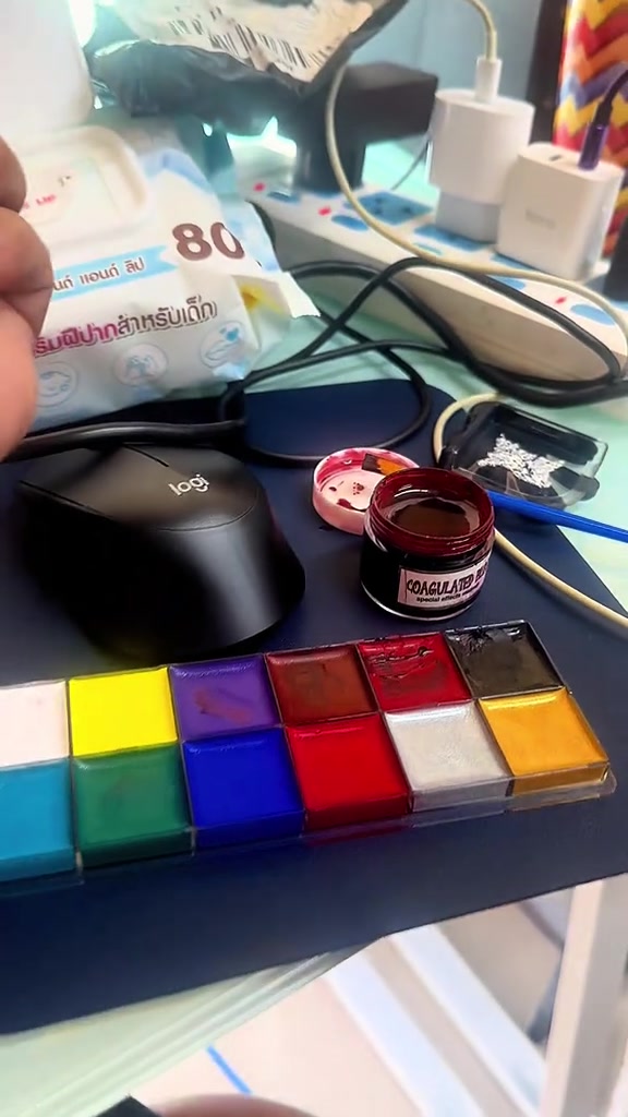 พาเลตต์สีครีมหลายช่องและกระปุกเจลสีแดงเข้มเปิดฝาวางบนโต๊ะทำงานข้างแพ็กทิชชู่เปียก