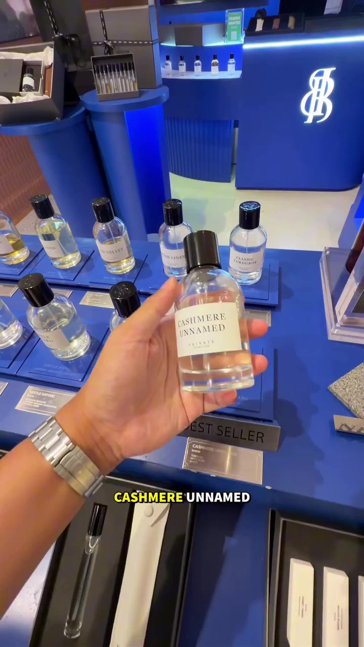 มือถือขวด BOROM Cashmere Unnamed เหนือป้าย best seller บนชั้นสีน้ำเงินของเคาน์เตอร์ มีขวดกลิ่นอื่นเรียงด้านหลัง