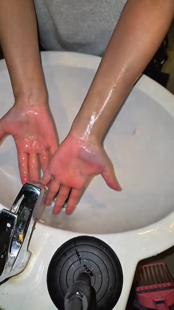 มือและแขนทั้งสองข้างกำลังล้างน้ำในอ่างล้างหน้าสีขาวหลังล้างเลือดปลอมออก
