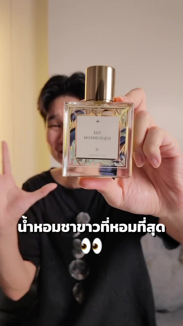 ขวดน้ำหอมแก้วฝาทองฉลากลายพิมพ์สีน้ำเงินทองถูกชูขึ้นหน้ากล้อง ฉากหลังเบลอ