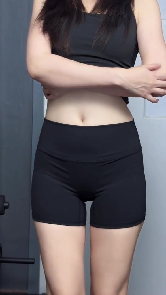 ด้านหน้าของผู้หญิงตั้งแต่คอลงมาใส่ชุดเซ็ตออกกำลังกายสองชิ้นสีดำยืนในห้อง