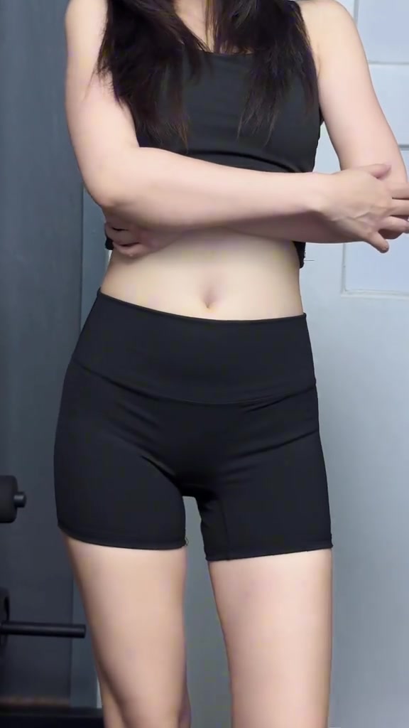 มุมมองเฉียงของผู้หญิงตั้งแต่คอลงมาใส่ชุดเซ็ตออกกำลังกายสีดำเห็นรอบเอวและทรงกางเกง