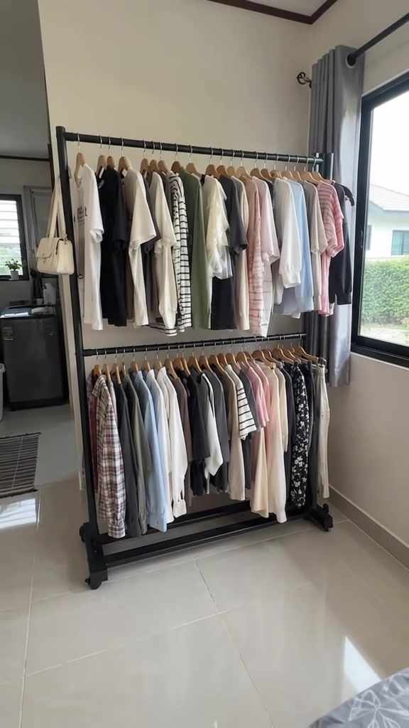 ราวแขวนเสื้อผ้าเหล็กสีดำสองชั้นแขวนเสื้อเต็มทั้งสองราวตั้งชิดผนังข้างหน้าต่าง