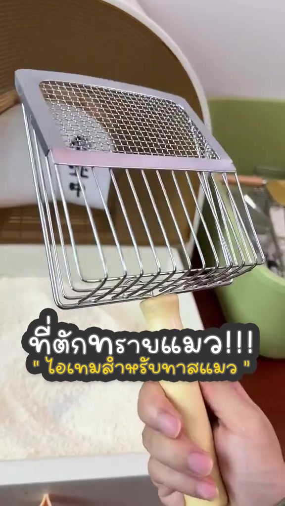 ที่ตักทรายแมวสแตนเลสแบบสองโซนด้านบนตาข่ายถี่ด้านล่างซี่ห่างด้ามไม้ถูกยกโชว์เหนือกระบะทราย