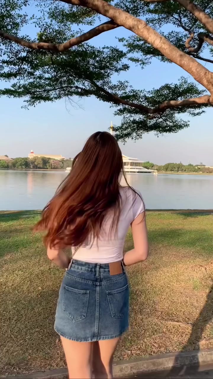 ด้านหลังของสาวสวมเสื้อยืดสีขาวกับกระโปรงยีนส์สั้นสีกลางยืนริมสนามหญ้าริมทะเลสาบ