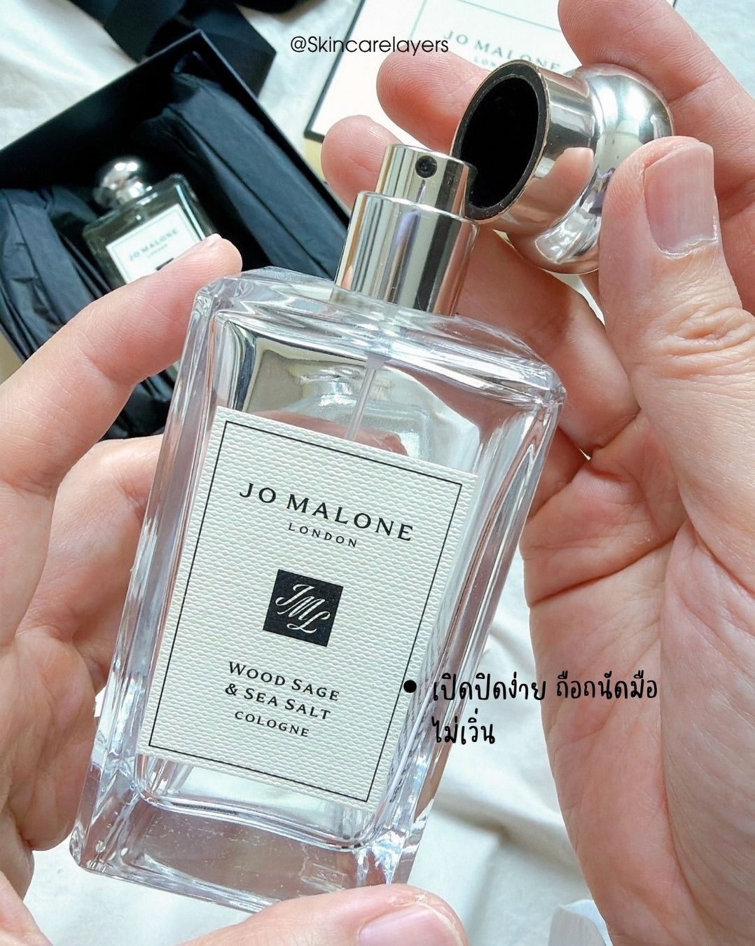 มือเปิดฝาขวด Jo Malone Wood Sage & Sea Salt เห็นหัวสเปรย์สีเงินและฉลากด้านหน้าขวด