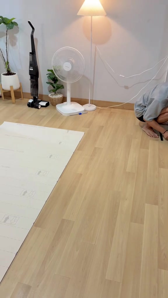 พื้นกระเบื้องยางลายไม้ระหว่างปู มีแผ่นด้านหลังสีขาววางค้างบนพื้นบางส่วนและส่วนที่ปูเสร็จแล้ว