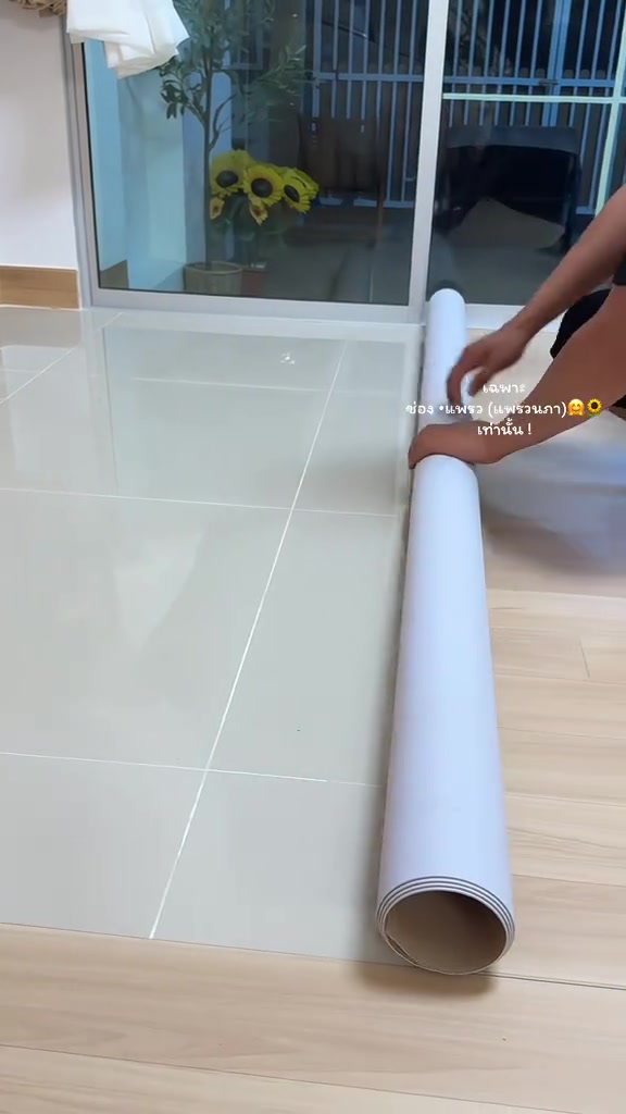 มือกำลังคลี่กระเบื้องยางพีวีซีแบบม้วนด้านหลังสีขาวลงบนพื้นกระเบื้องสีขาวเดิม
