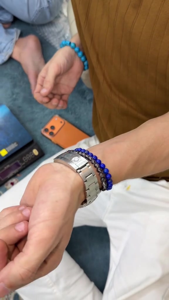 กำไลลูกปัดหินสีน้ำเงินสองเส้นสวมซ้อนกับนาฬิกาสายโลหะบนข้อมือ