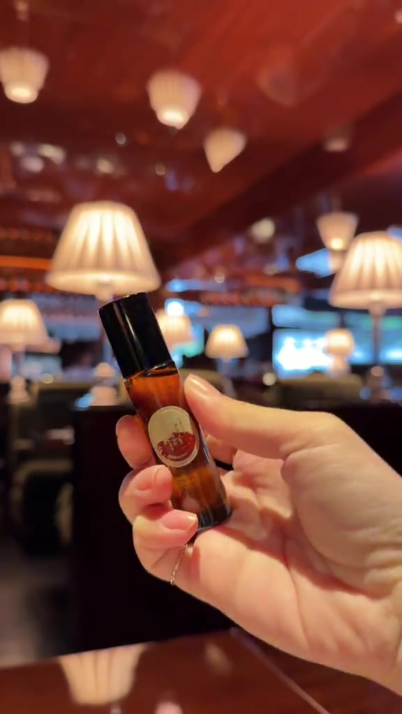 มือถือขวด Karmakamet Authentic Perfume Body Oil สีอำพันฝาดำขนาดเล็กในคาเฟ่แสงอุ่น