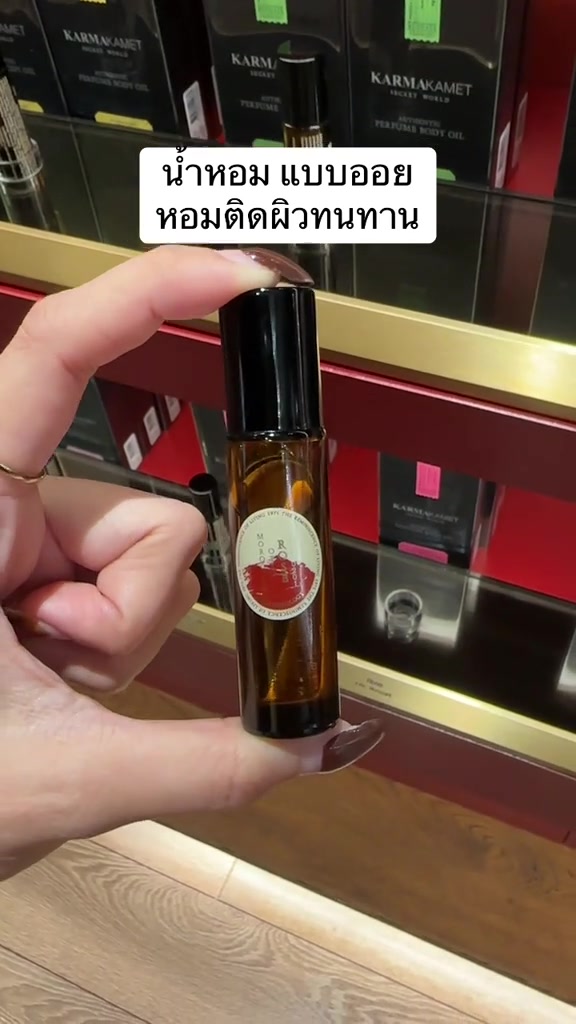 มือถือขวด Karmakamet Perfume Body Oil สีอำพันหน้าชั้นวางกล่องผลิตภัณฑ์ในร้าน