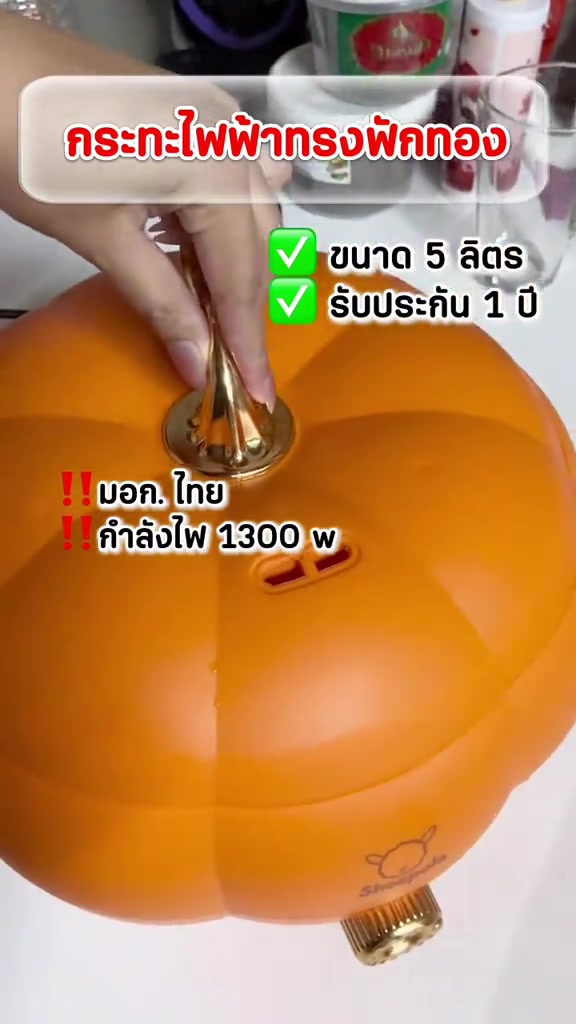 มือกดหูจับฝาสีทองของกระทะไฟฟ้าทรงฟักทองสีส้ม เห็นช่องเสียบสายไฟสองรูและรูระบายไอน้ำบนตัวหม้อ